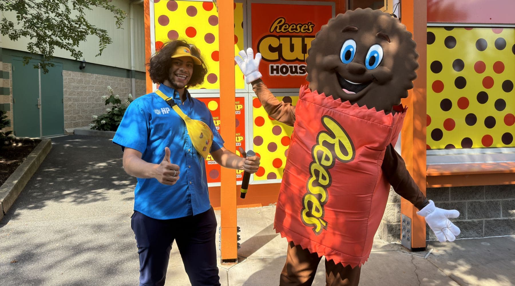Hershey Team Member posing with Reese Character in front of Reese's Cup House attraction.