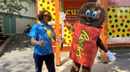 Hershey Team Member posing with Reese Character in front of Reese's Cup House attraction.
